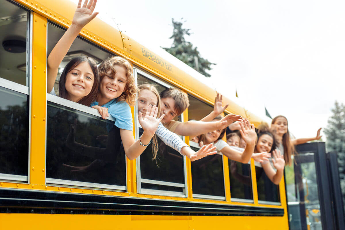 Children leaning out of school bus window and waving